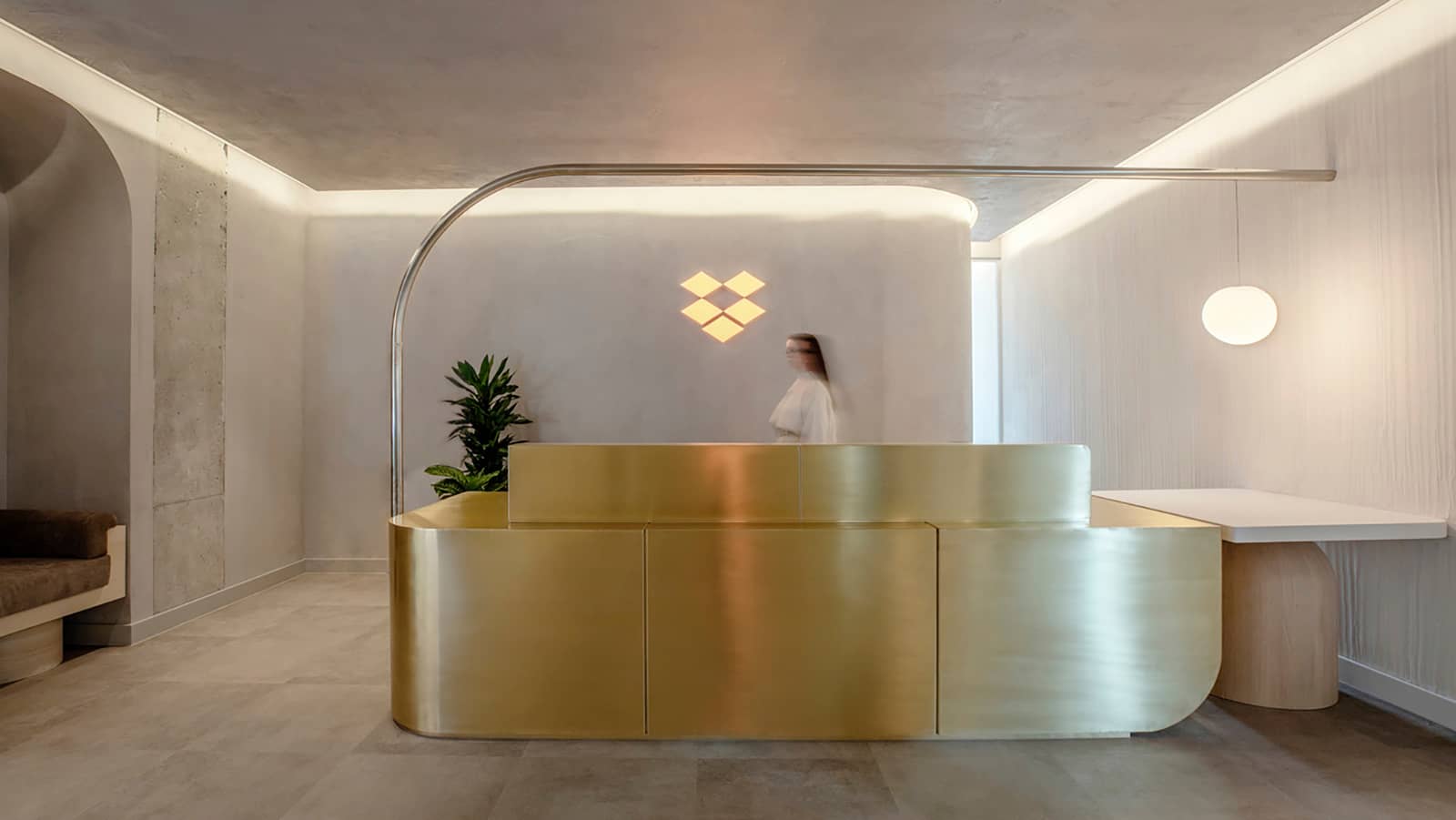 The reception area at Dropbox's Dublin offices featuring a golden reception desk, and rounded, white walls with a lit logo display.